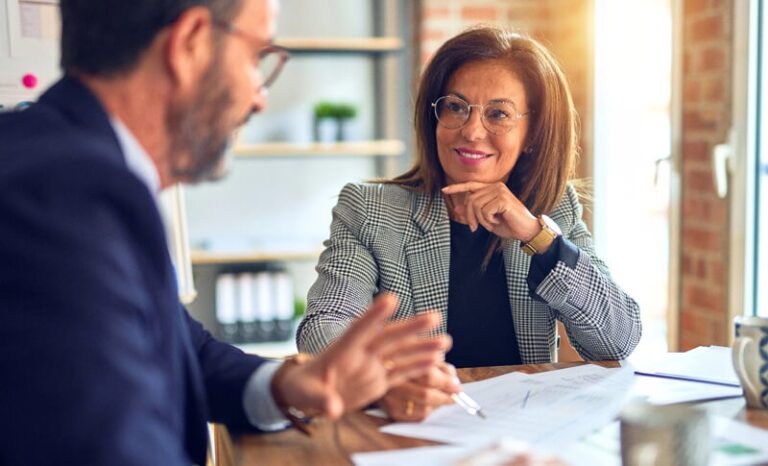 Man and woman in business clothing talking while sitting at table with papers