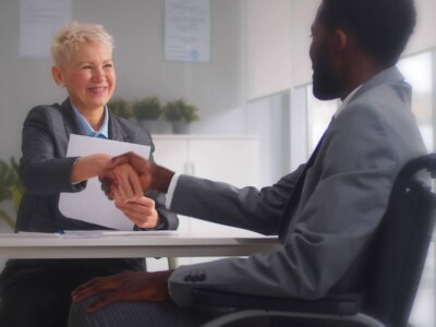 Male disabled job candidate and mature female employer shaking hands and smiling at camera.