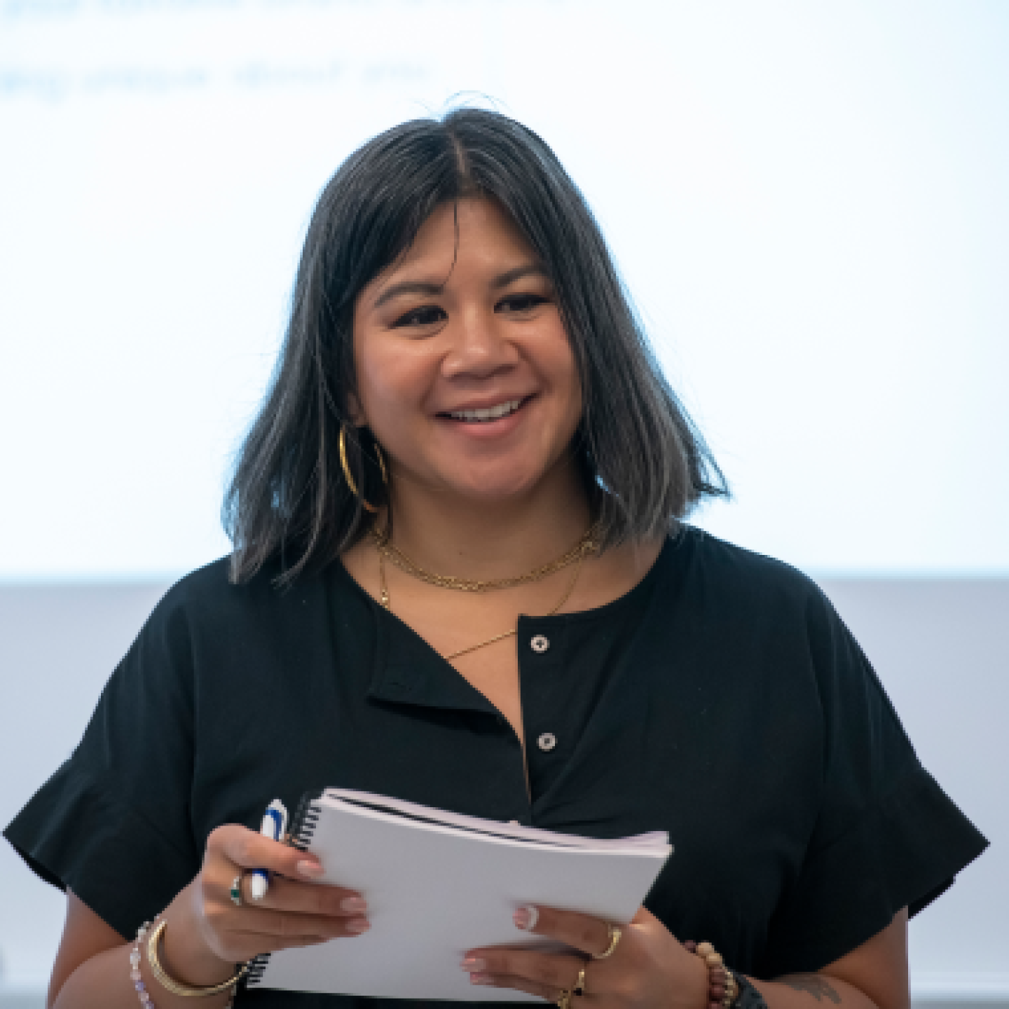 A female Yeshiva University professor is standing in front of a classroom while holding a notepad.