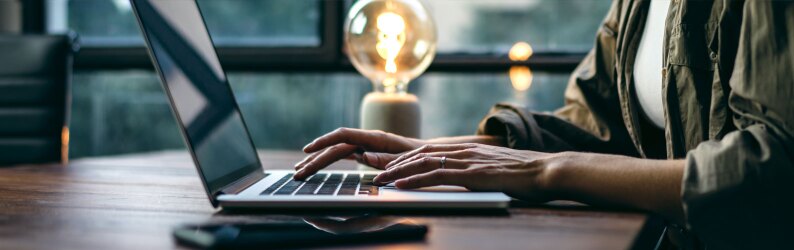Person typing on a laptop next to a lighted lamp