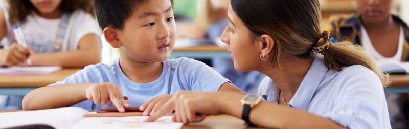 Teacher helping student in classroom with an assigned reading.