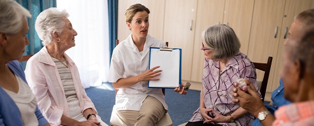 medical professional with clipboard in hand speaking to a group of elderly people