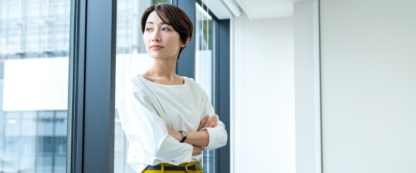 A professional woman in a white shirt looks out of a window as she considers best employee retention strategies