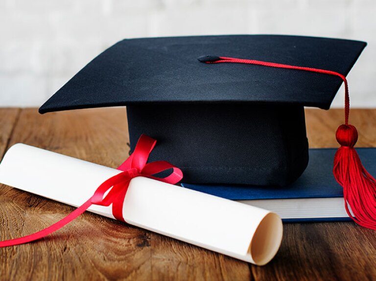 Graduation cap and diploma laying on top of a wooden table