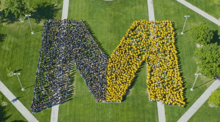 Students in blue and yellow standing in the shape of UC Merced logo