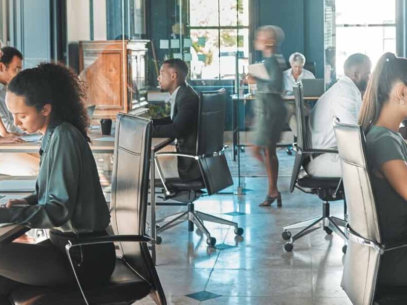 Corporate business people working on their laptops at desks in busy marketing office space.