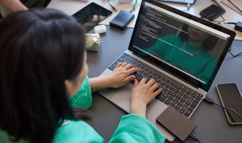 Focus on the hands of a young female student, typing on a laptop keyboard while analyzing and decoding data on screen