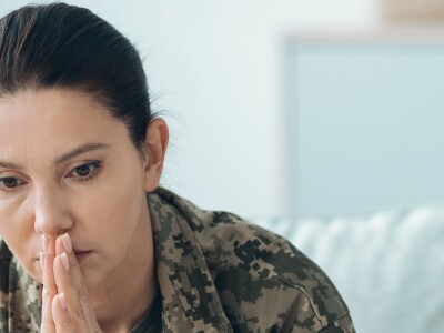 A woman wearing a military uniform sits on a couch with a thoughtful expression.