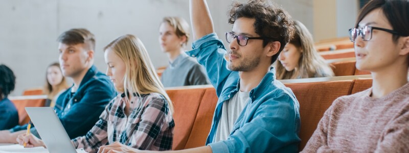 Surrounded by classmates, a university student raises his hand during a lecture.