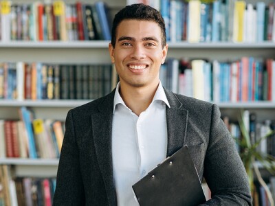 A confident school principal standing in front of a large library bookshelf