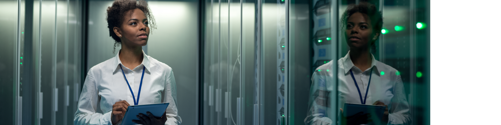 African American woman using tablet while walking in corridor of data center and checking hardware on server racks