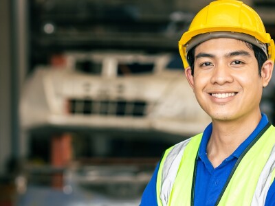 An engineer wearing a hard-hat smiles in a factory work setting