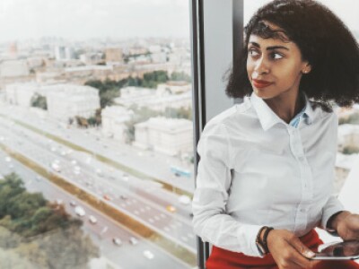 Professionally dressed woman sitting next to window holding tablet