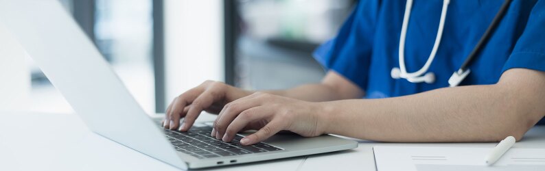 A healthcare professional is typing on a laptop, updating medical records, and conducting research.