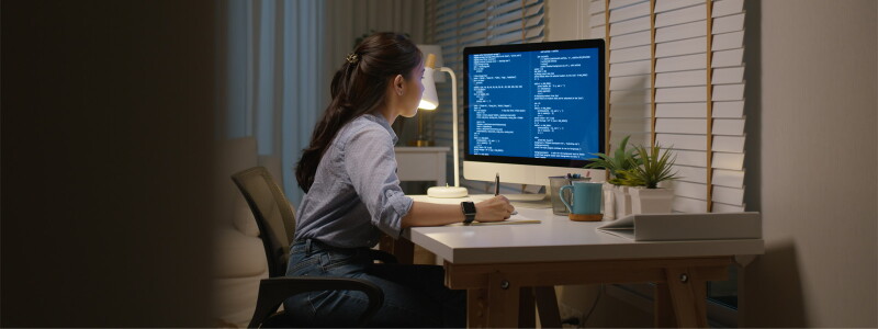Young woman sits at a desk, studying a computer screen and taking notes.