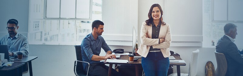 Confident woman business leader standing at desk with arms crossed for success