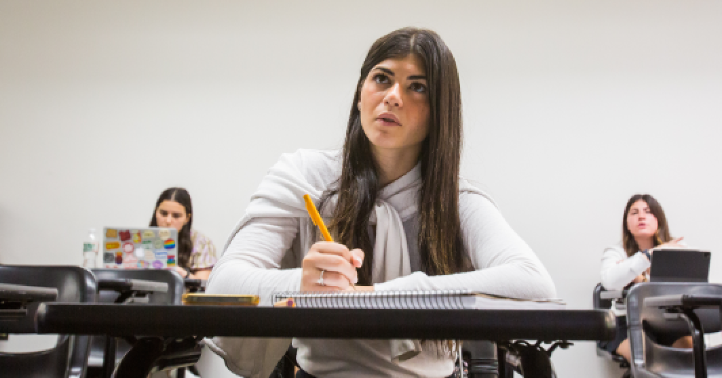 A female Yeshiva University student is sitting in class while taking lecture notes.