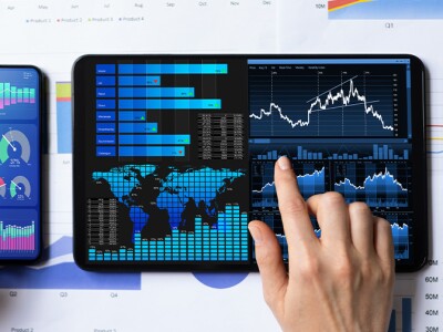A person's hands working on multiple phone and tablet screens, which rest on bar-graph documents