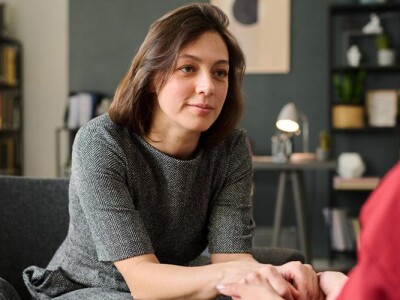 Female mental health counselor sitting opposite to client, holding hands in supportive gesture during a session