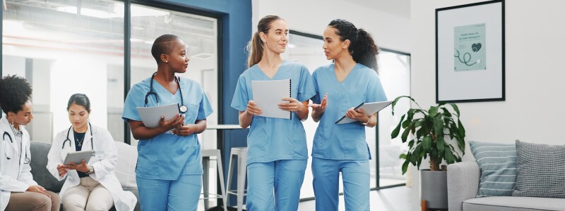 Three nurses walk through a clinic discussing a patient's case
