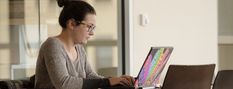 A student sits at a table working on her laptop
