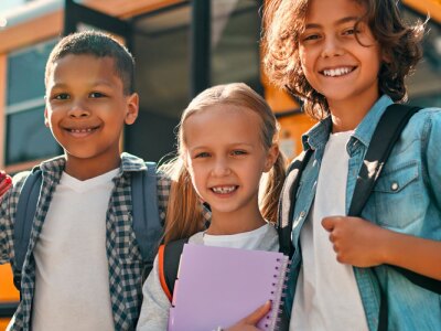 Group of school children stand together in front of a school bus.