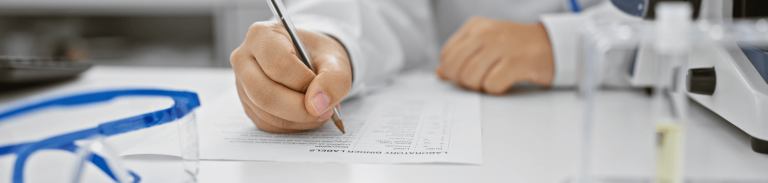 Hands of clinical research professional filling out form near microscope and lab goggles