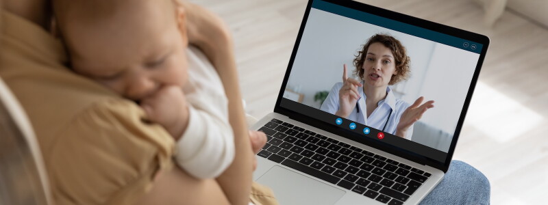 A mother holding her baby speaks with a physician via telehealth call.