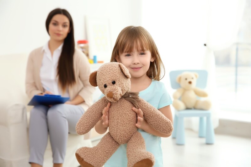 social worker sitting on a bench observing a child holding a teddy bear