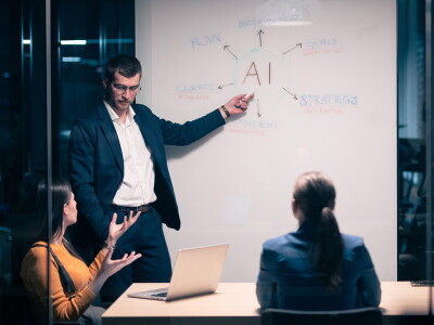 Marketing professionals in a meeting room at a table and a whiteboard with 'AI' written on it.