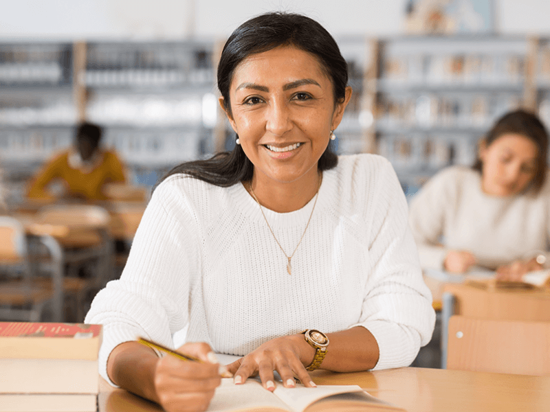 Woman writing in library at table with books
