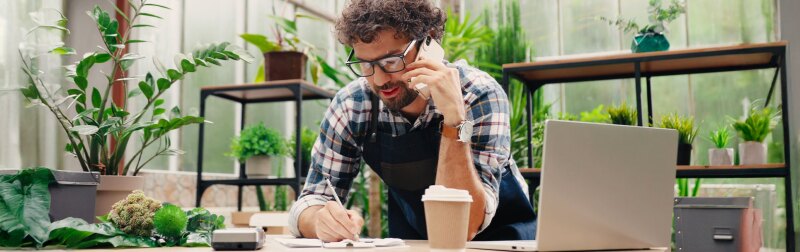 Businessman in a small floral shop on a cellphone taking order details