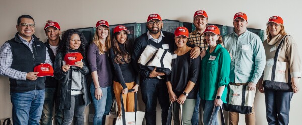 Online MBA student group stands holding read SU ballcaps