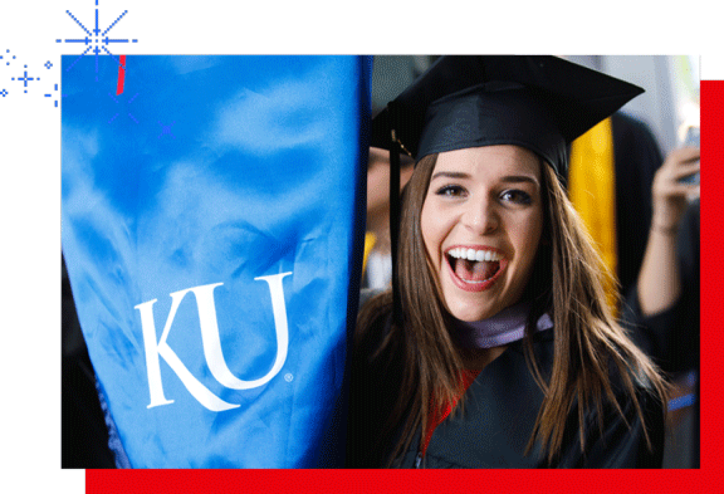 Smiling graduate in cap and gown holding a KU banner during a graduation ceremony.