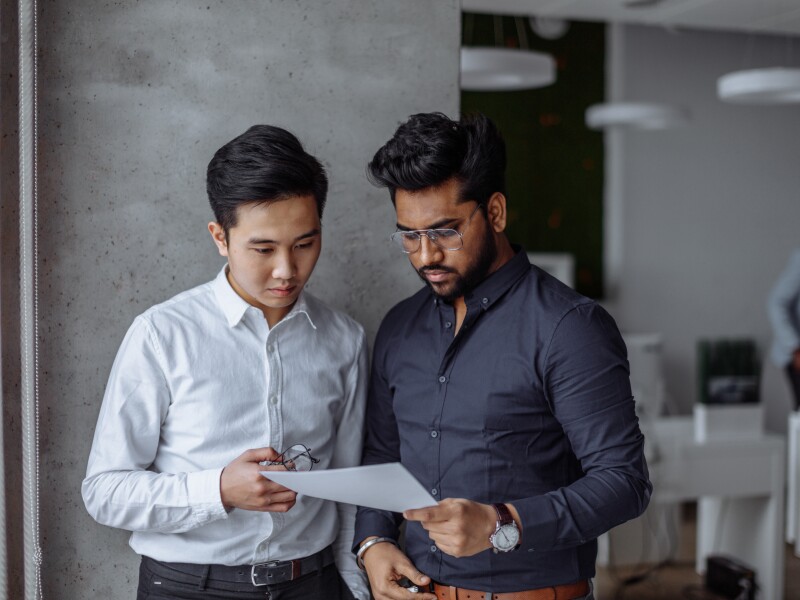 Mix raced male business partners analyzing reports against grey wall