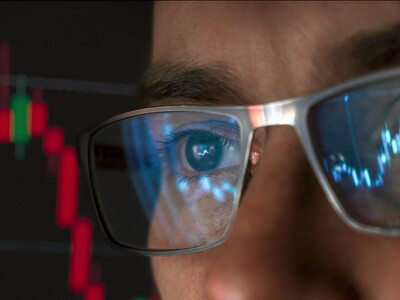 A close-up view of a man wearing glasses, with data charts reflecting on the lenses