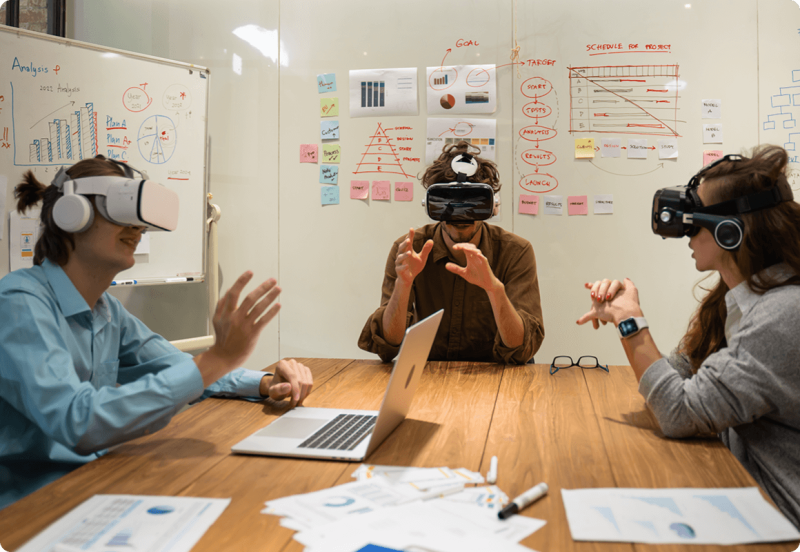 Two men and one woman using AR headsets in meeting room with graphs drawn on whiteboards