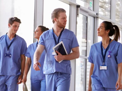 Four nurses talking while walking through a sunny hallway