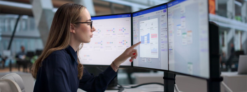 Young female marketer designs personalized email campaigns on three large computer screens.