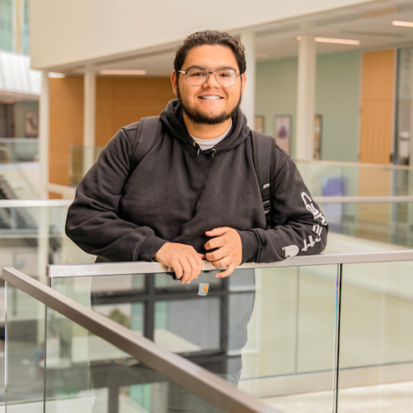 A smiling male CSUMB student leaning on a glass railing.