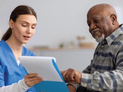 Woman in scrubs talks reviews a document with a man in a wheelchair.