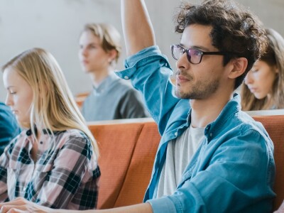 Surrounded by classmates, a university student raises his hand during a lecture.