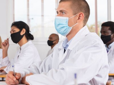 Focused man studying in classroom with medical colleagues in protective face masks for disease prevention during training program.