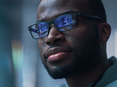Close up of a man working on computer, lines of code reflecting on his glasses.