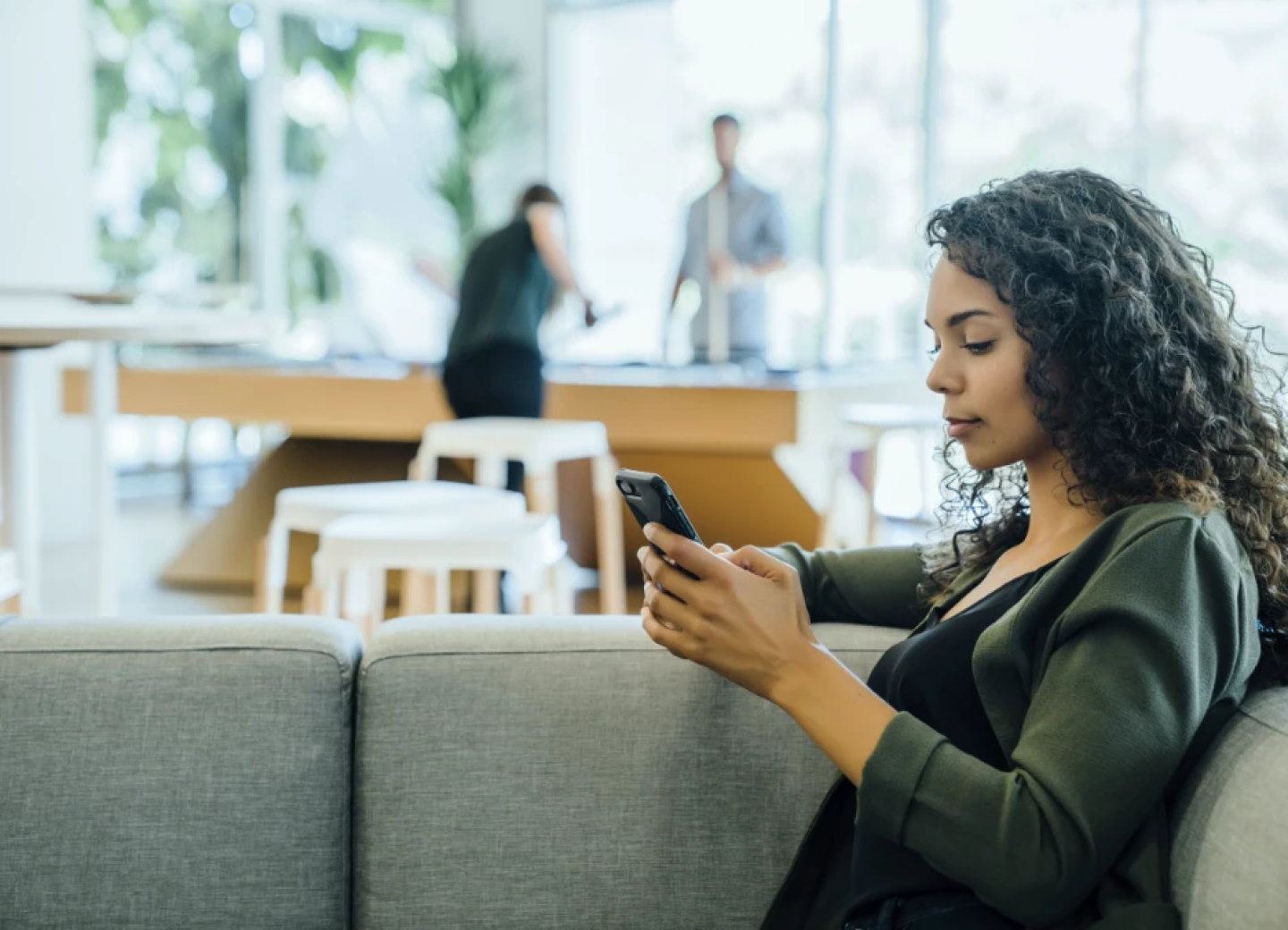 Woman seated on couch in office lounge texting on phone