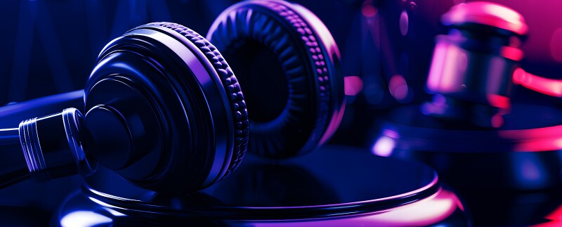 Close-up of a gavel and a pair of headphones illuminated by purple and blue lights
