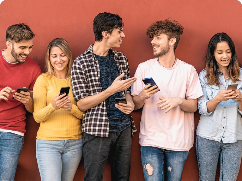 group of young adults standing by a wall with phones in their hands