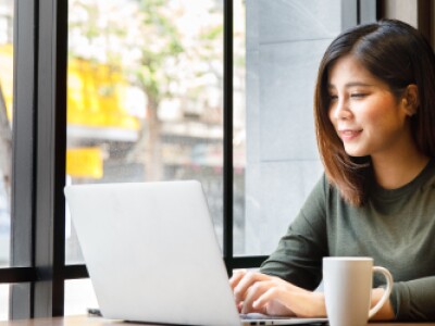 woman in green sweater sitting at laptop in front of window