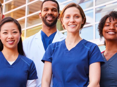 Smiling team of diverse nursing professionals standing together outside a hospital.