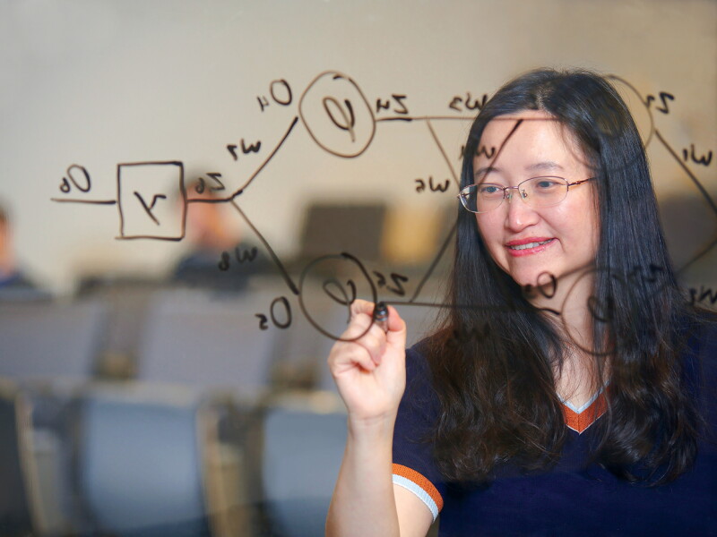 Woman writing a diagram on a glass board in a classroom.
